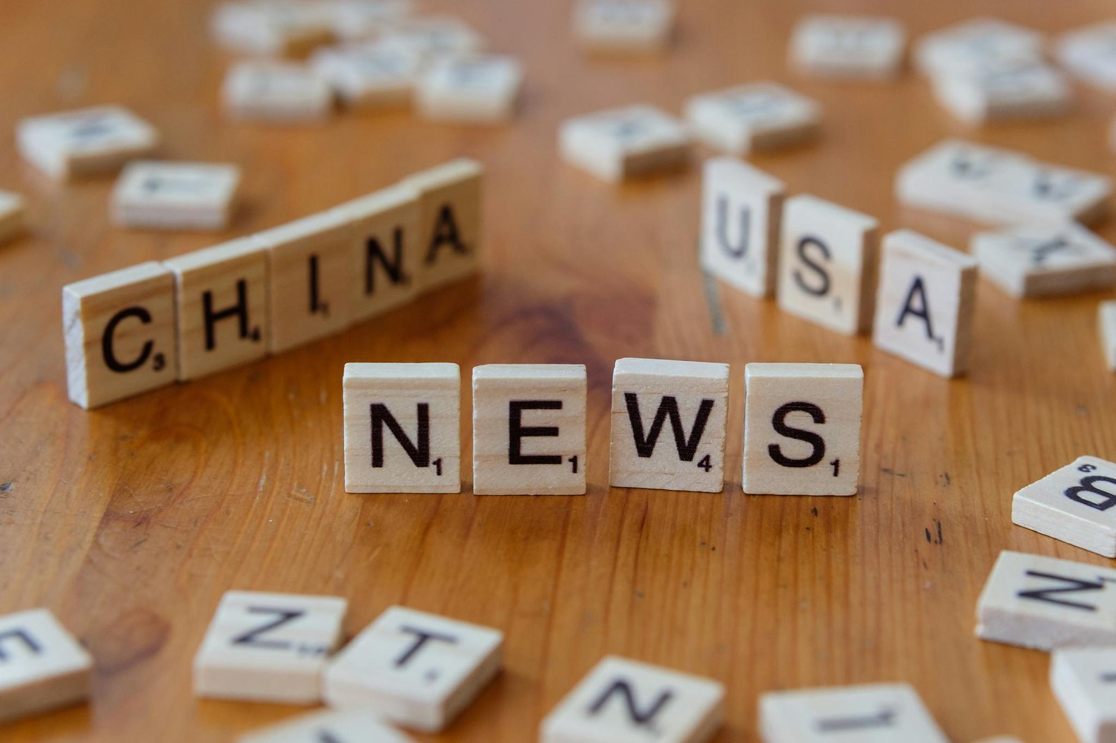 Wooden Scrabble tiles spelling 'NEWS' with 'CHINA' and 'USA' on a wooden surface.